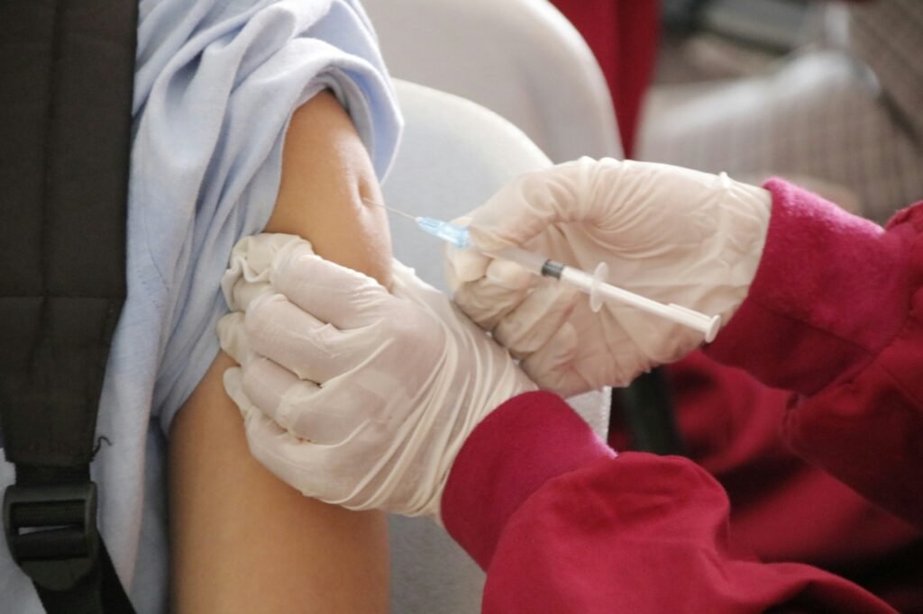 Person receiving a vaccination injection in their upper arm from a healthcare professional wearing gloves.