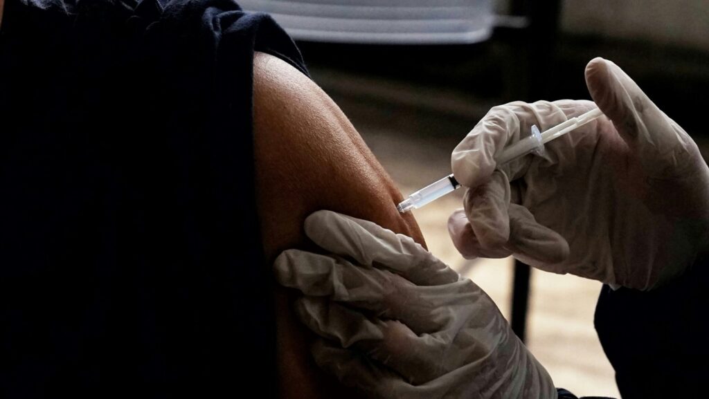 Healthcare professional giving a patient a vaccination injection in the upper arm.